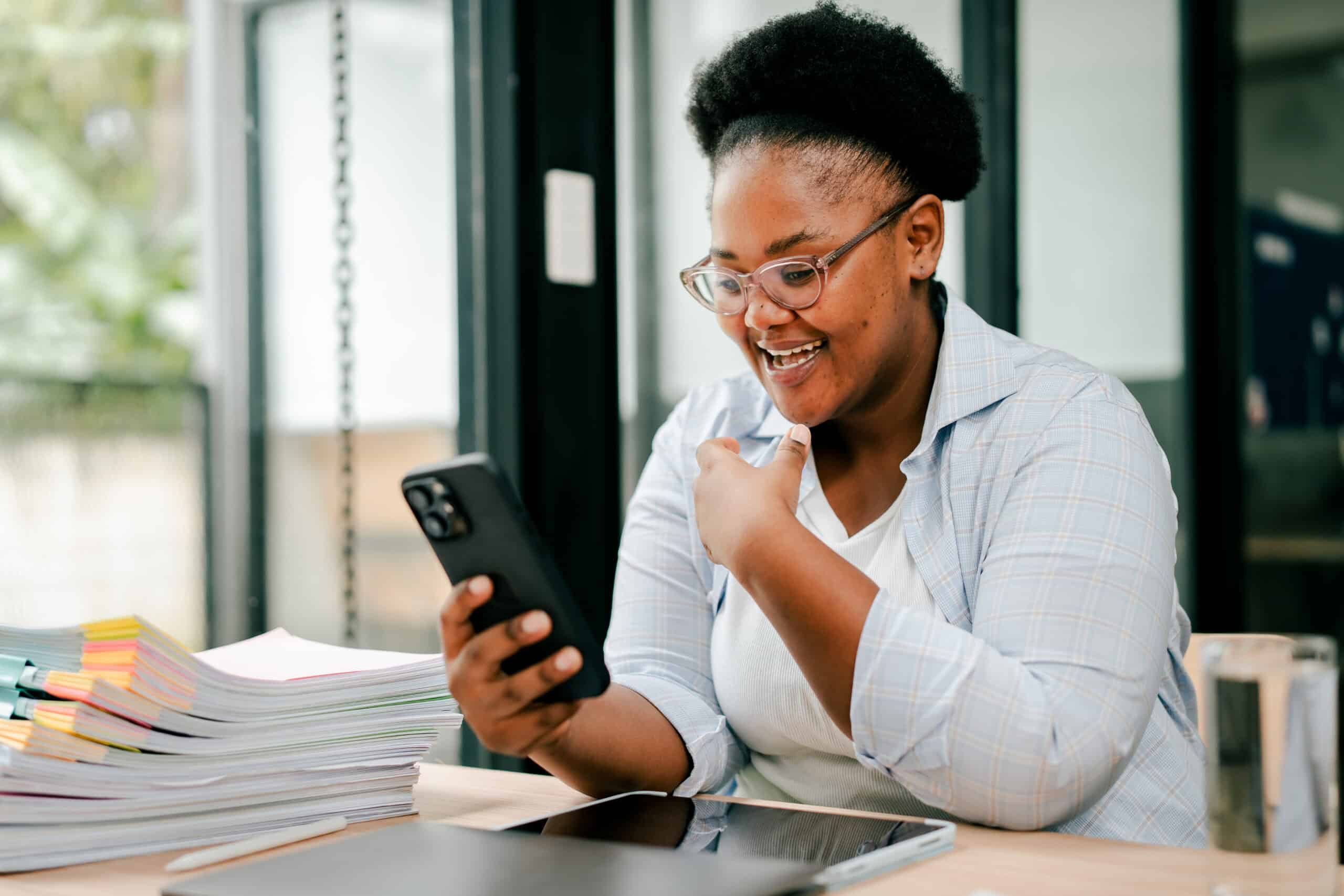 Black woman smiling using smartphone in office